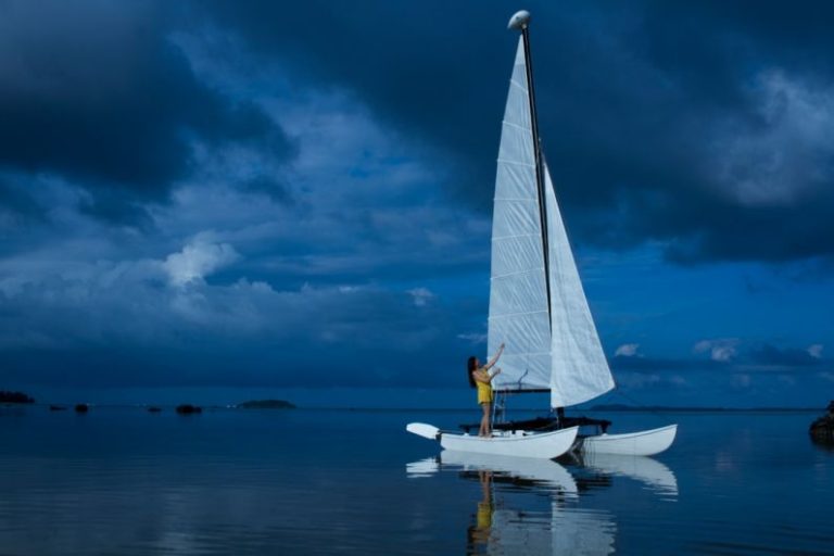 Watercraft - woman standing in white sailing boat on blue sea during night time