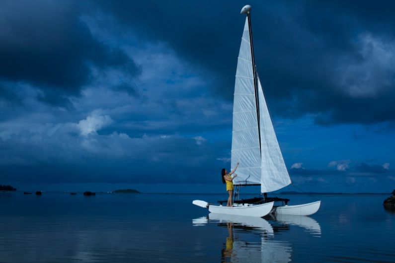 Watercraft - woman standing in white sailing boat on blue sea during night time