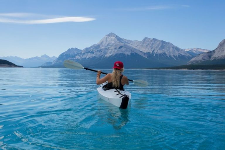 Rowing - woman wearing red hat riding on white kayak facing mountain alps